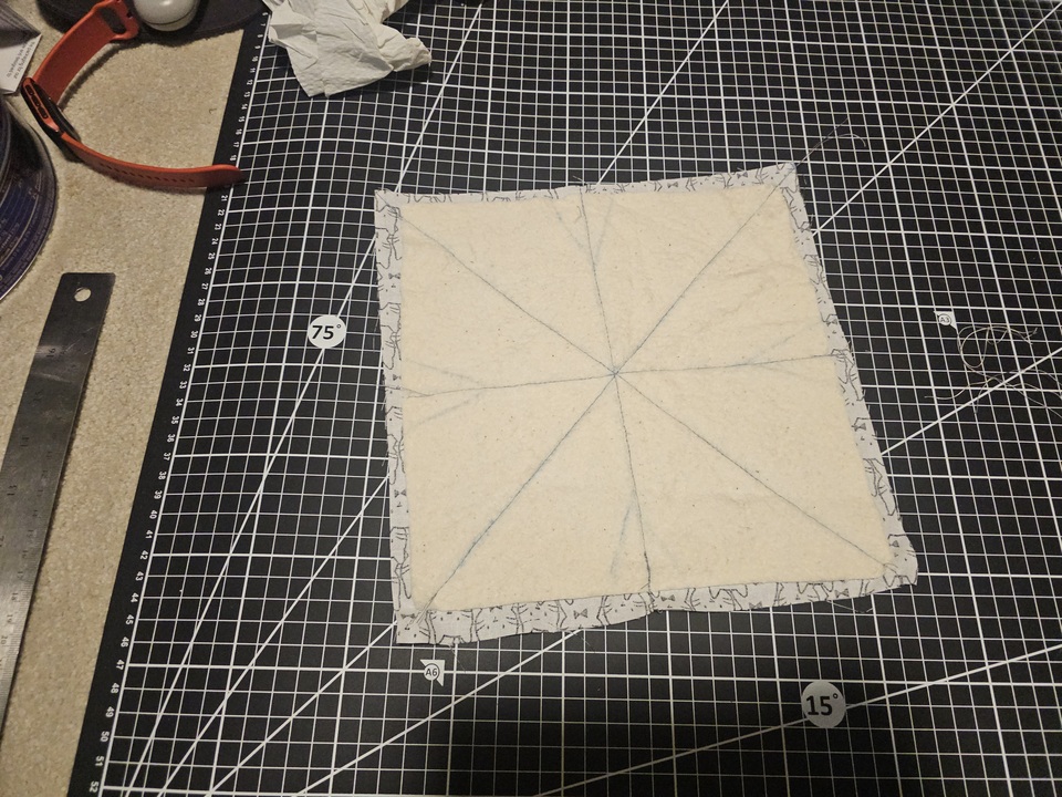 one square of cat fabric and batting sewed together with a cross and diagonals on a cutting mat