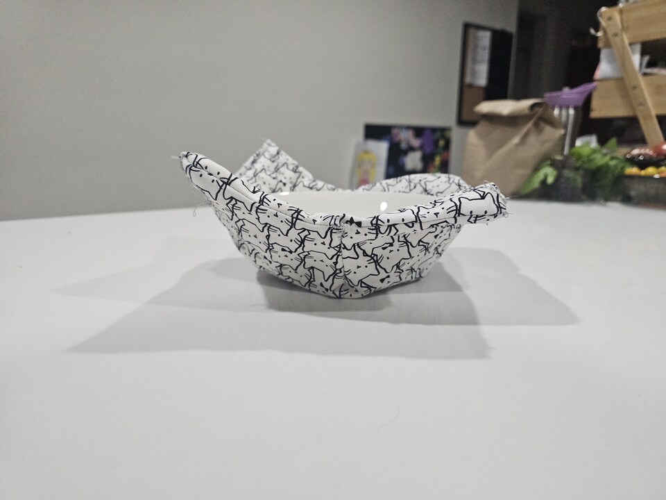 a cat fabric bowl cozy with a white bowl in it, on a white table - side profile
